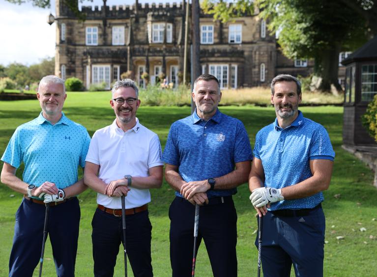 Four men stood on a golf course holding golf clubs