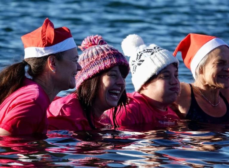 Four people wearing bobble hats in a lake