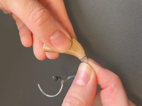 A person screwing or unscrewing the tubing from a hearing aid