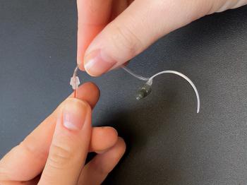 A person inserting a cleaning rod into the hearing aid tubing