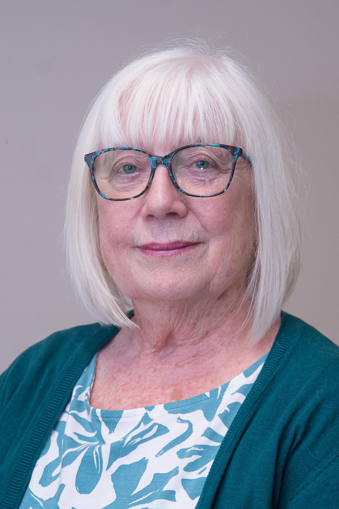 Valerie Ball is wearing glasses, a white and green patterned top and green cardigan