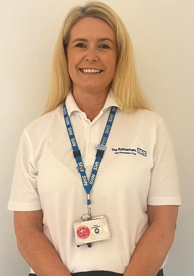 Cath is smiling. She has a white polo shirt with the Trust's logo and a blue NHS lanyard