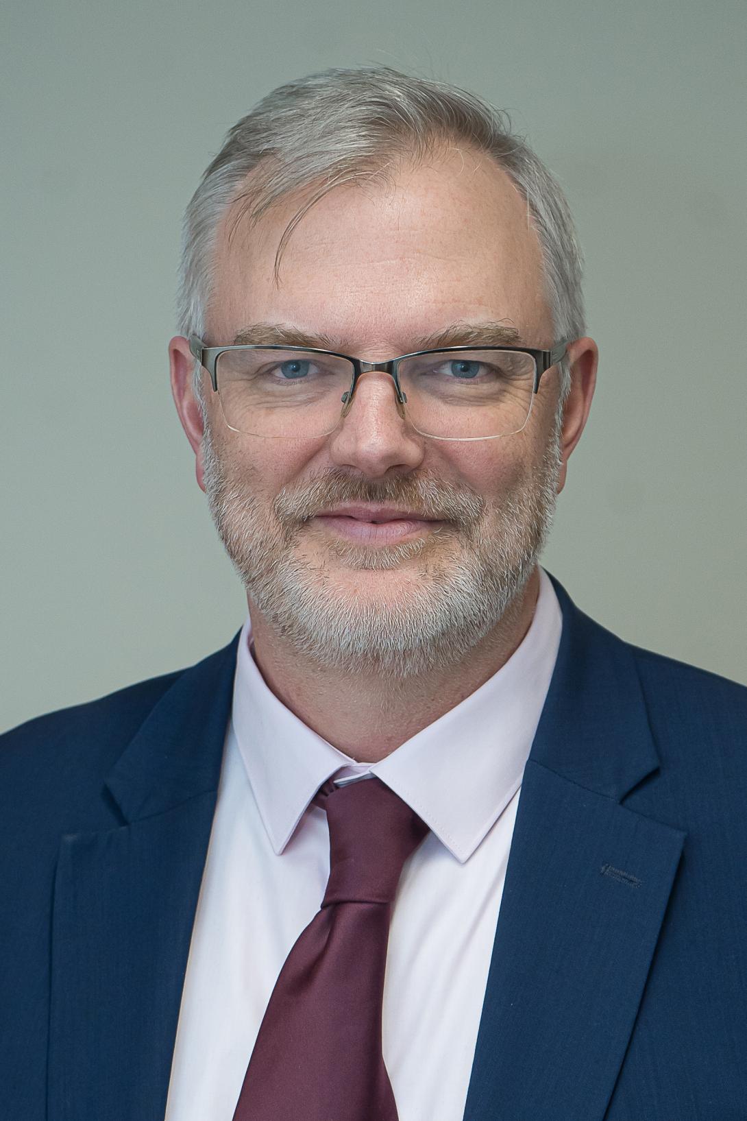 Bob is wearing glasses, a blue suit with a burgundy tie